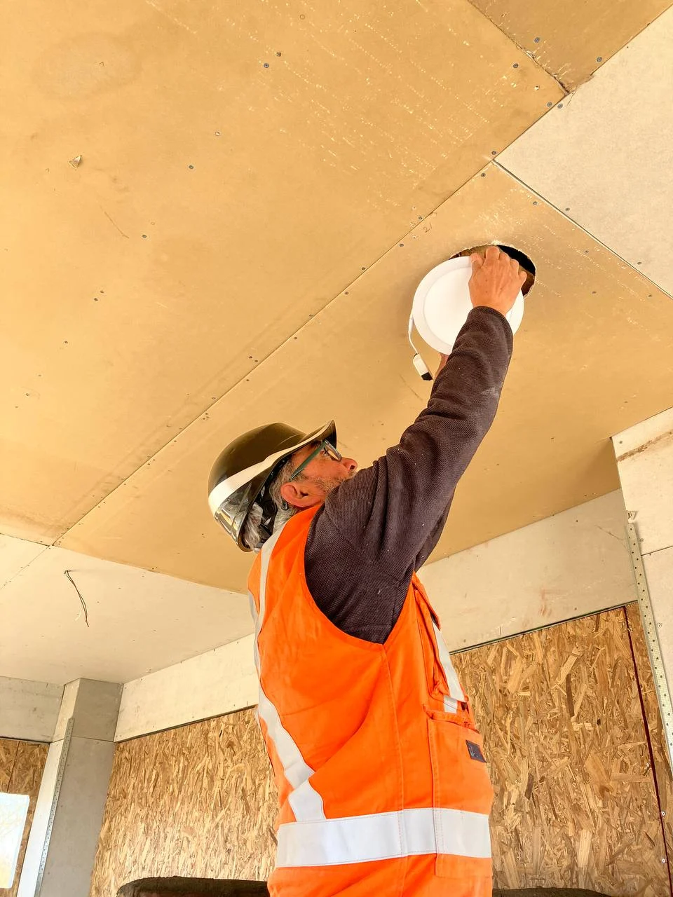 Maestro eléctrico instalando iluminación en un cielo de madera